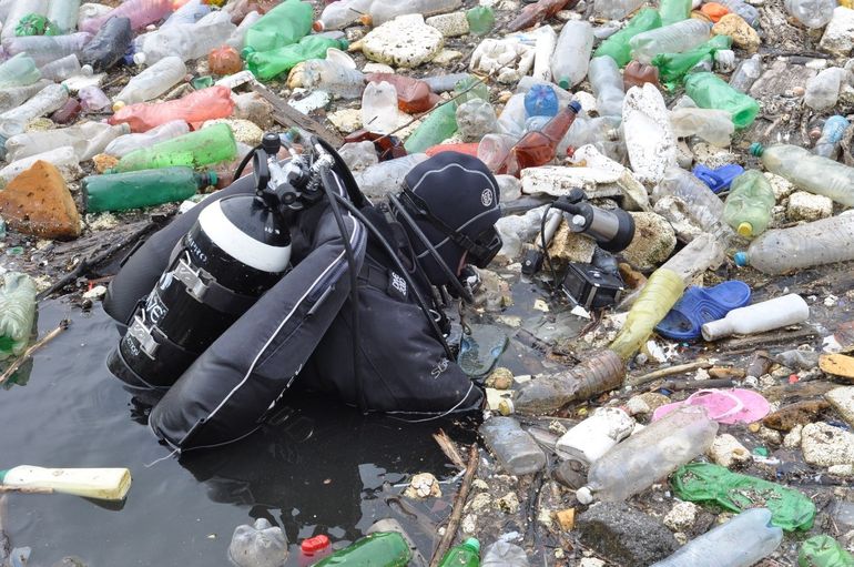 potápač vo vode obklopený plastovými fľašami 	