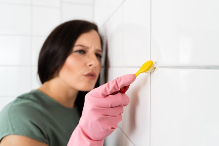 Žena čistí kachličky v kúpeľni.