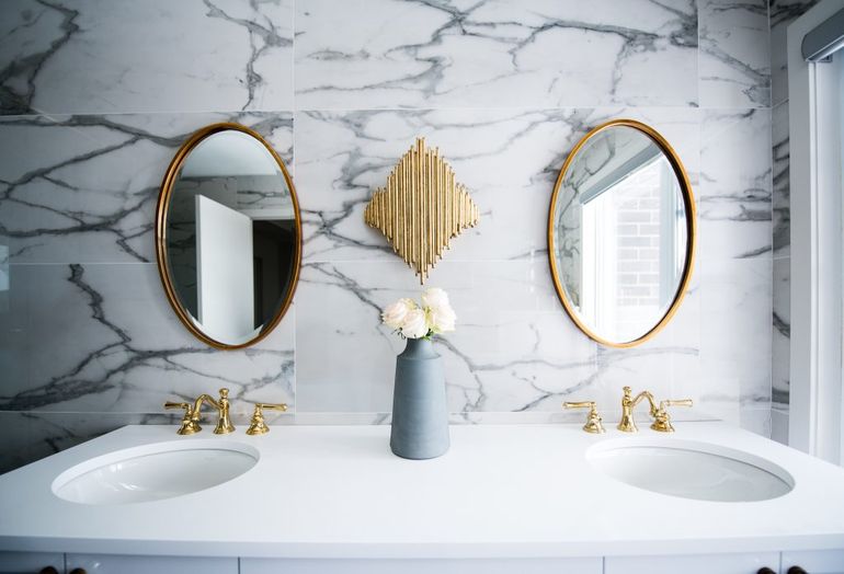 Luxusná kúpeľňa s dvomi umývadlami a okrúhlymi zrkadlami v zlatom prevedení.