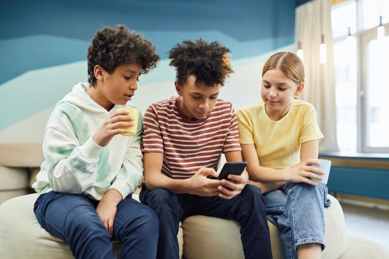 tri deti sediace na gauči a pozerajú do mobilu 
