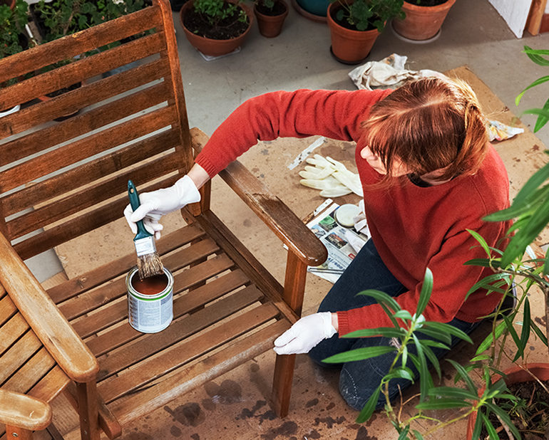 žena vonku maľuje drevenú stoličku 
