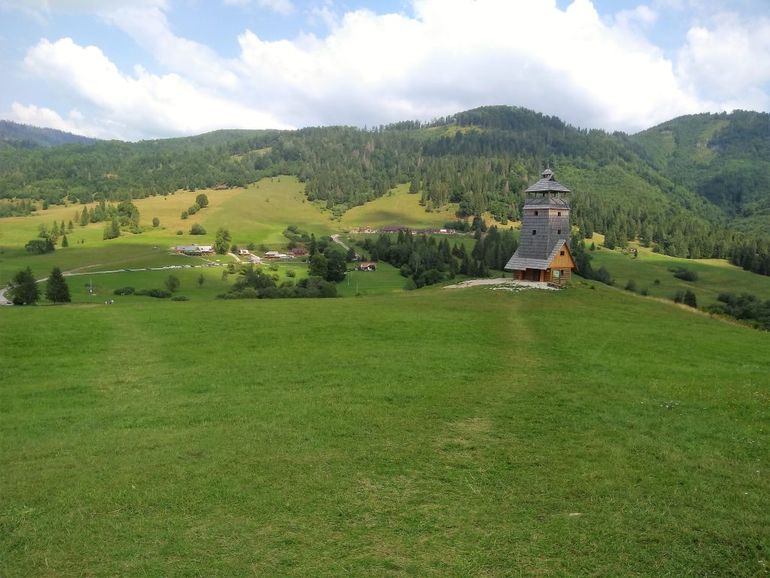 Malebná drevená veža pre turistov v prírode obklopenej lesmi a lúkou.