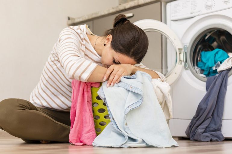 Žena spí s bielizňou v práčovni pri práčke.